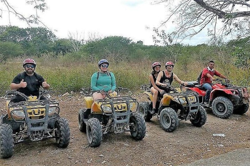 Four people on ATVs on a dirt path with vegetation in the background. 2