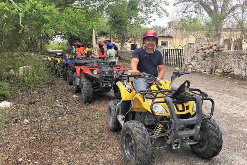 A person on a yellow ATV, with other ATVs and people in the background. 1