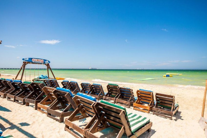 A beach with wooden lounge chairs and a signboard. 5