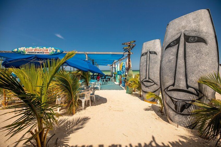 A beach with large stone sculptures, a sign for Silvet Beach Club, and palm trees. 4