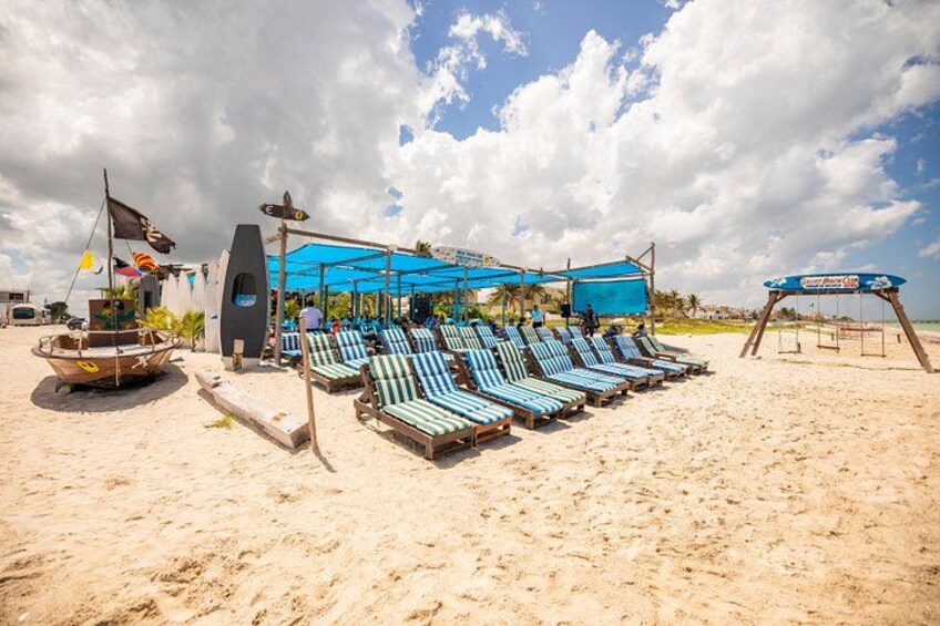 A beach with lounge chairs, a boat, and a shaded area. 2
