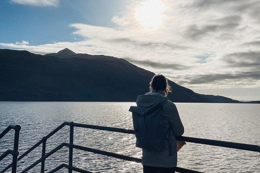 Une personne se tient sur un quai, surplombant un lac paisible, avec des montagnes en arrière-plan. 3