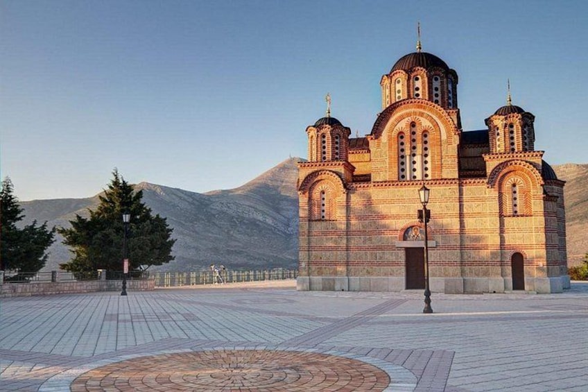 Una iglesia con tres cúpulas, una plaza empedrada y una montaña al fondo. 1