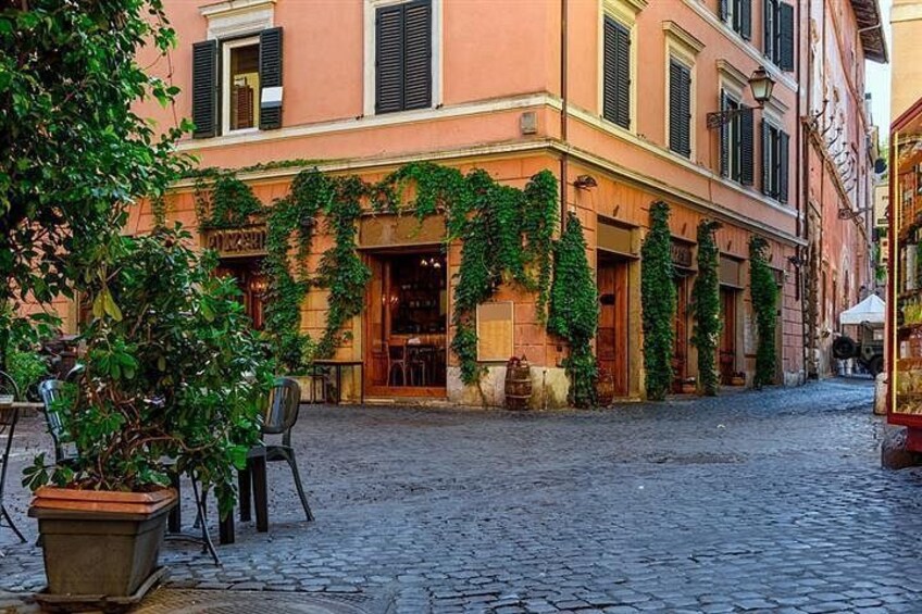 A cobblestone street with a building covered in green ivy, outdoor seating, and a potted plant. 5