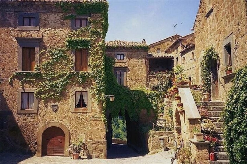A historic stone building with ivy-covered walls, a wooden door, and a staircase leading to an upper level. 3