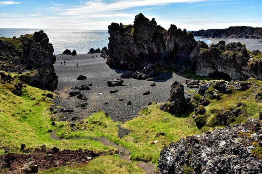 A rocky beach with people walking, surrounded by cliffs and a clear sky. 3