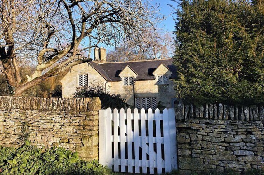 A stone house with a white picket fence, surrounded by trees and a stone wall. 1