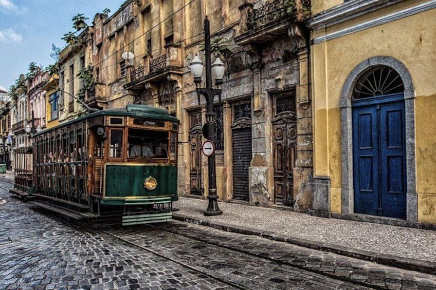 Eine grüne Straßenbahn auf Kopfsteinpflaster, historische Gebäude und eine blaue Tür. 3