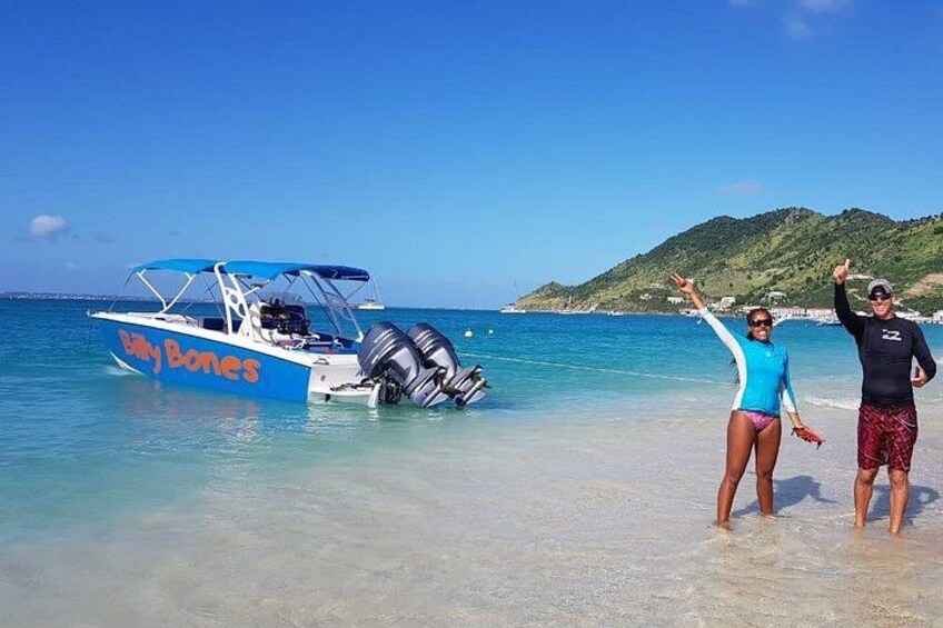 Un bote llamado 'Baby Bones' en una playa con aguas claras y un paisaje montañoso al fondo. 1