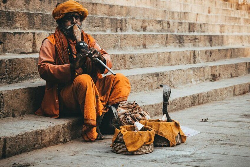 A person sitting on stone steps, dressed in orange, with a bag and a stick. 1