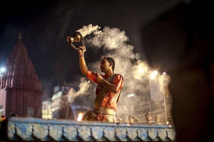 A person performing a ritual with a brass vessel, surrounded by smoke and a temple structure in the background. 4