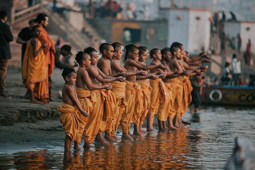 Monks in orange robes standing in a line by a river. 2