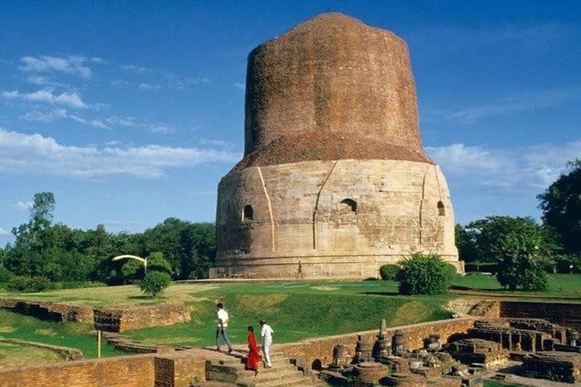 A large, ancient stone structure with a rounded top, surrounded by a grassy area with ruins and trees. 3