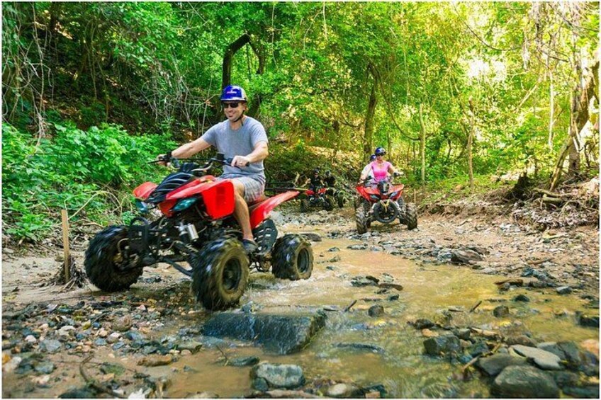 Two people riding ATVs on a rocky path in a forested area. 3