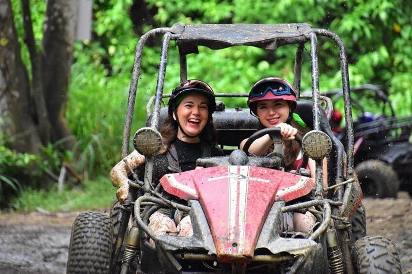 A red off-road vehicle with two people wearing helmets, driving through a muddy terrain. 1