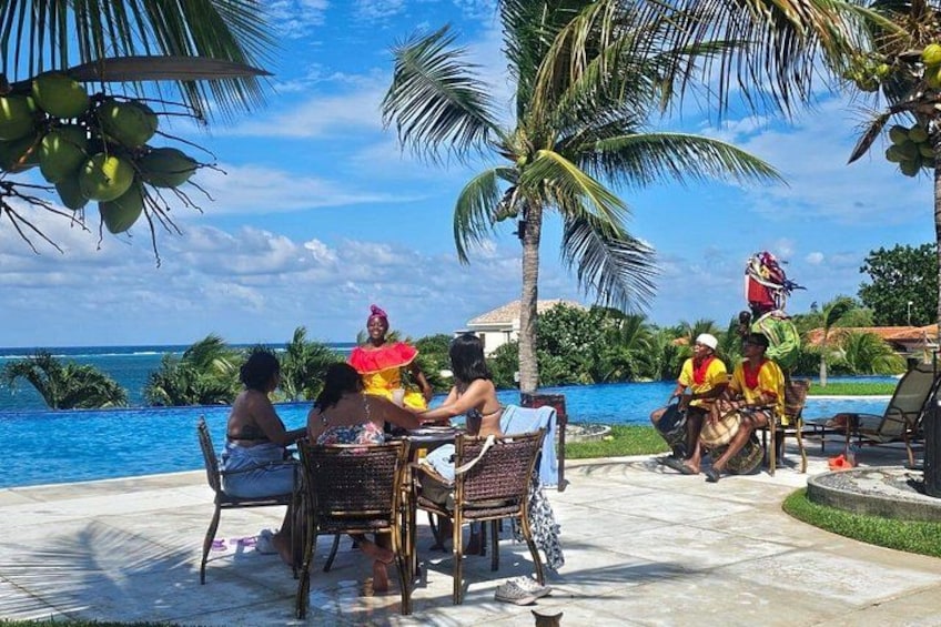A group of people sitting at a table by a poolside, palm trees, and a clear blue sky. 4