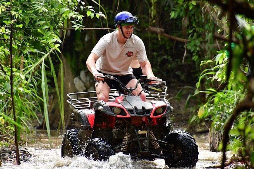 A person riding an ATV through a water body surrounded by dense greenery. 3