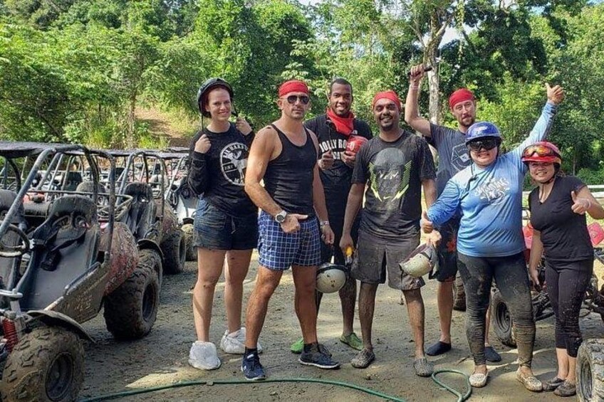 A group of people standing in a muddy outdoor area with off-road vehicles in the background. 5