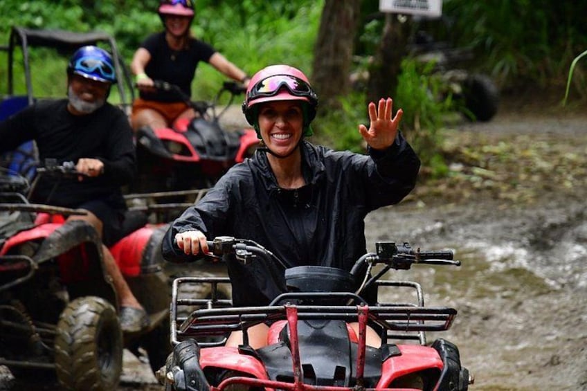 A person on a red ATV in a muddy terrain, waving. 3