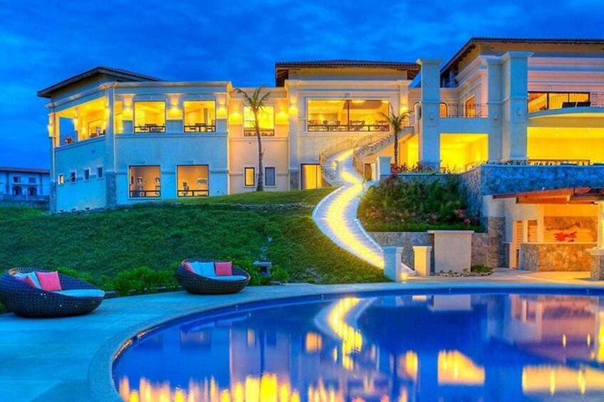 A luxurious infinity pool overlooks a pristine beach with turquoise water. Guests sip fresh coconuts and tropical drinks while lounging under palm shades. 2
