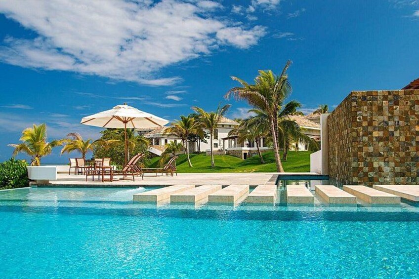 A swimming pool with clear blue water, palm trees, and a resort building in the background. 5