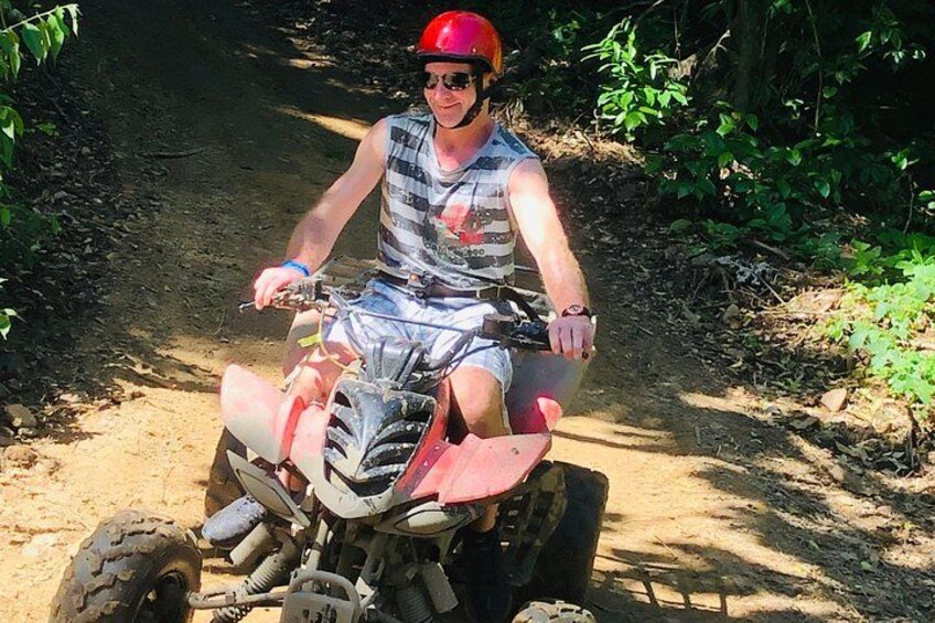 A person riding a quad bike on a dirt path surrounded by greenery. 3