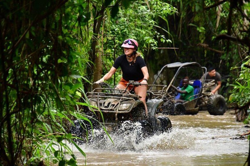 Eine Person fährt mit einem Quad durch einen Fluss, umgeben von dichter Vegetation. 5