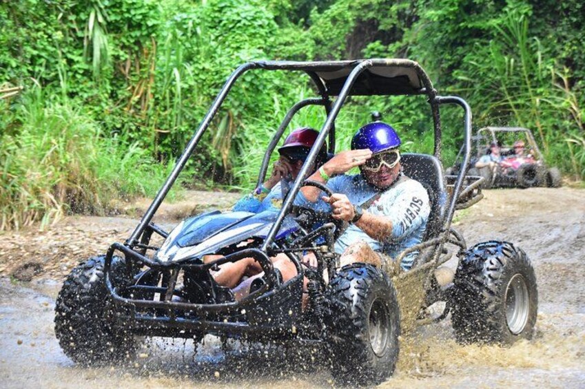 A person driving a four-wheeled vehicle through a muddy area with water splashing around. 2