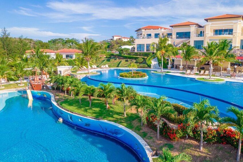 Ein Resort mit mehreren Schwimmbecken, Palmen und Gebäuden. 2