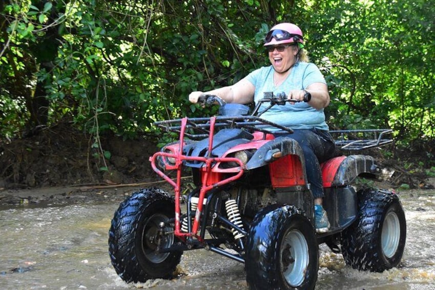A person riding a red ATV through a shallow water crossing. 4