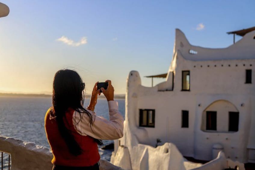 A person taking a photo of a white building with a curved roof by the sea. 5