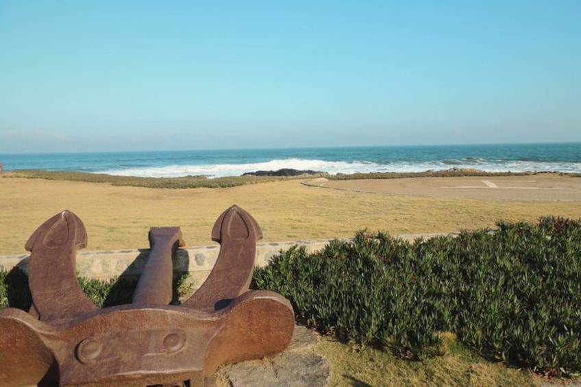 A coastal landscape with a sandy beach, ocean waves, and a rusty anchor in the foreground. 2