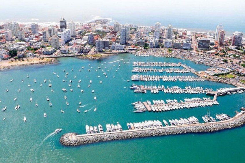 Un paysage urbain côtier avec un port de plaisance rempli de bateaux, une longue jetée et de hauts immeubles. 2