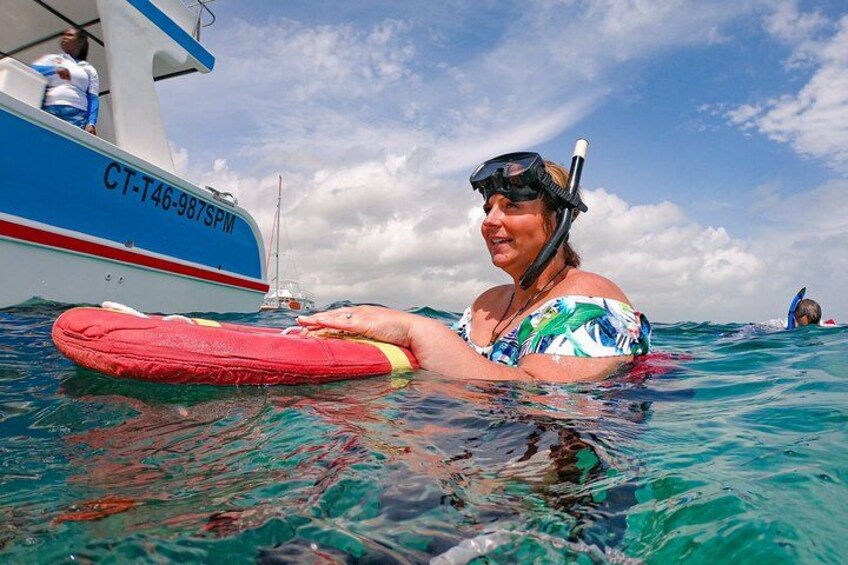 A person in a blue and white swimsuit floating on a red flotation device in clear blue water, with a boat in the background. 3