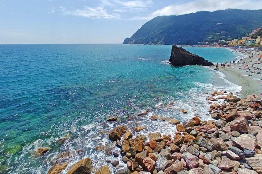 Una spiaggia rocciosa con acque turchesi cristalline, una grande formazione rocciosa e montagne sullo sfondo. 4