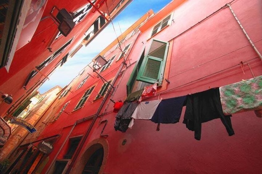 A narrow alley with red buildings, laundry hanging on lines, and a green window. 2