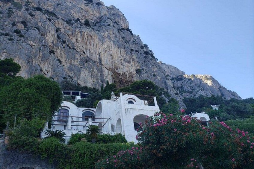 Un edificio blanco con arcos, rodeado de vegetación y un telón de fondo de montaña rocosa. 4