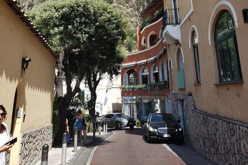 Una calle estrecha flanqueada por edificios, un coche aparcado y una persona caminando. 2