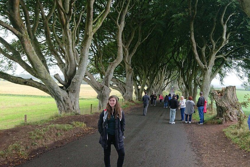 A pathway lined with trees, a person standing in the foreground, and a group of people walking in the background. 3