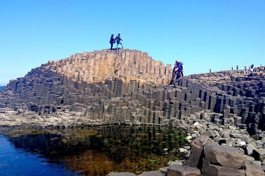 A rocky cliff with people standing on top and a body of water at the base. 3