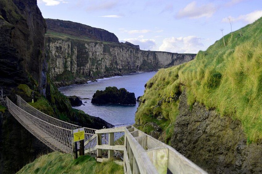 Eine Küstenlandschaft mit Klippen, einer Hängebrücke und einem Gewässer. 3