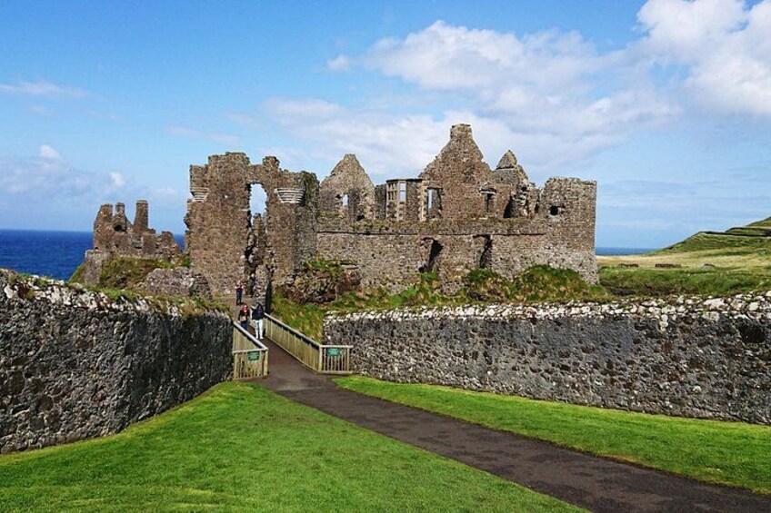 A historic stone castle with ruins, a grassy pathway leading to it, and the ocean in the background. 3