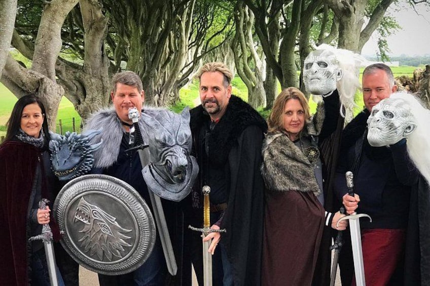 A group of people in medieval costumes holding swords and shields, standing in a park with trees. 2