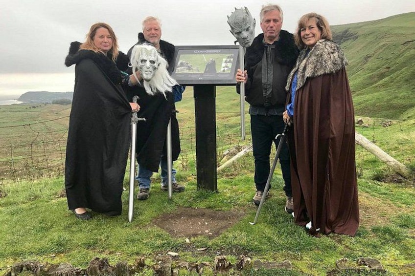 Un grupo de personas vestidas con trajes medievales de pie en un campo cubierto de hierba, con una señalización de fondo. 4