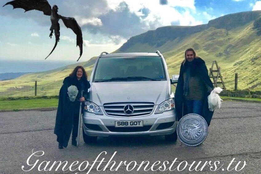 Un coche blanco con un calcomanía de dragón, una persona con capa y un perro blanco. 3