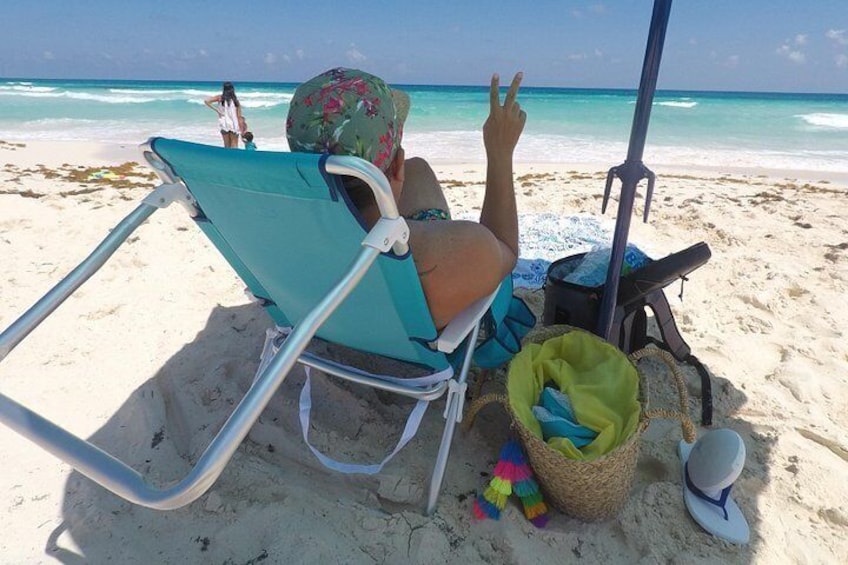 En person som sitter på en strandstol med ett parasoll, en strandstol, en soptunna och en strandväska. 2