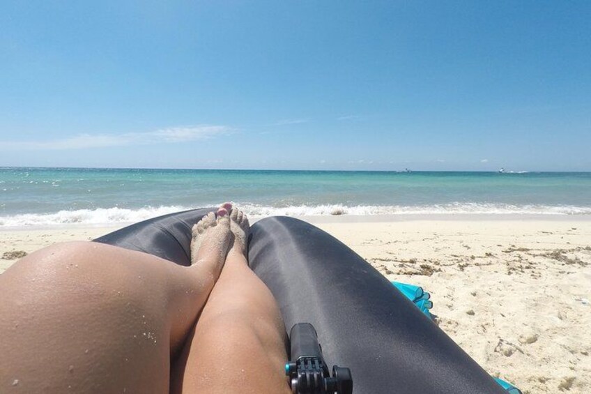 A person lying on a beach with a blue inflatable mattress, facing the ocean. 3
