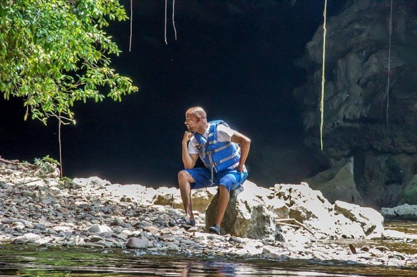 A person sitting on a rock by a river, wearing a blue life jacket. 5