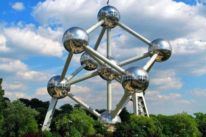 A metallic spherical structure with reflective surfaces, set against a backdrop of a partly cloudy sky and green foliage. 5