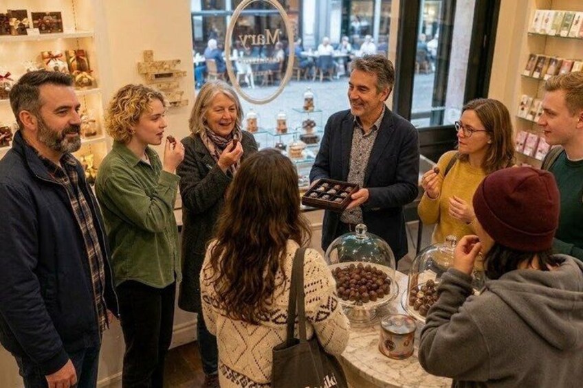 En grupp människor samlades runt ett bord med olika sorters mat, och en person stod och höll i ett fat med chokladpraliner. 3